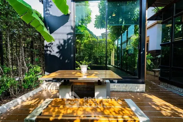 Modern outdoor patio with sleek glass walls and lush greenery, perfect for relaxation and entertaining.