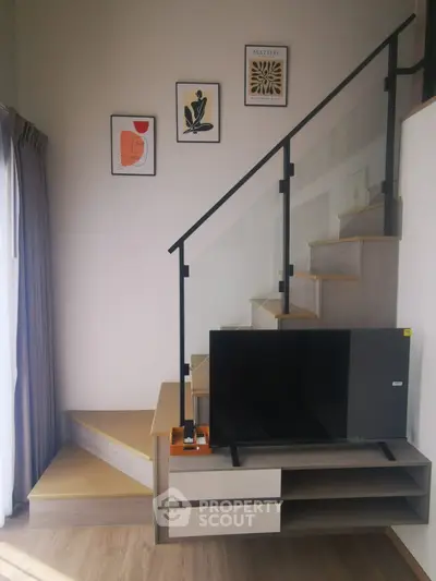 Modern living room with stylish staircase and TV unit, featuring contemporary wall art and natural lighting.