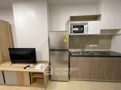 Modern compact kitchen with stainless steel fridge and microwave, adjacent to cozy living area with TV.