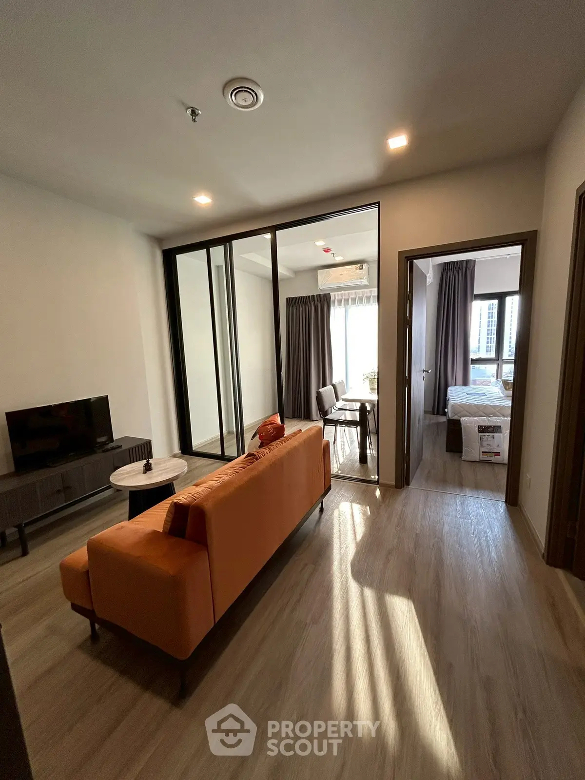 Modern apartment living room with orange sofa and sliding glass doors leading to a bedroom.