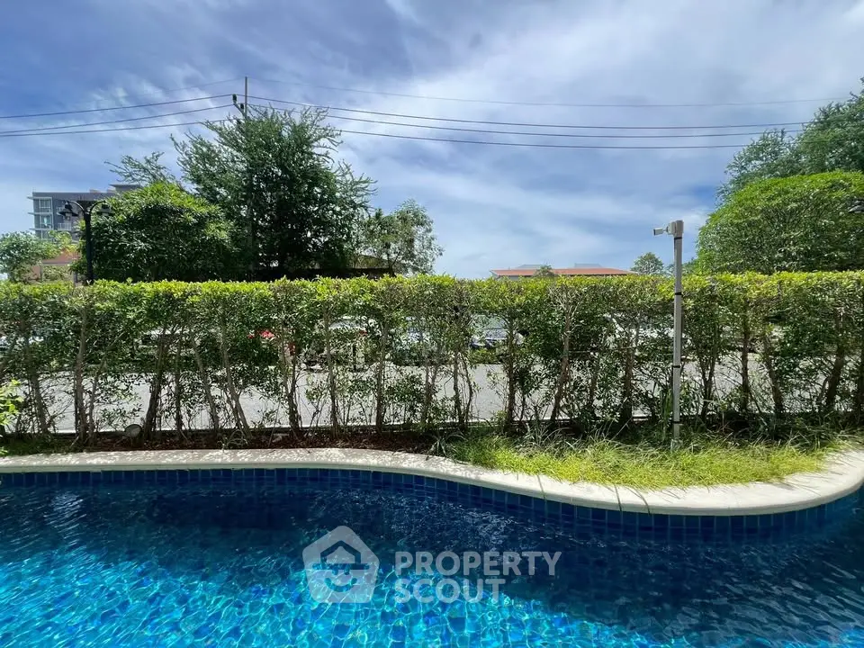 Luxurious poolside view with lush greenery and clear blue skies, perfect for relaxation.