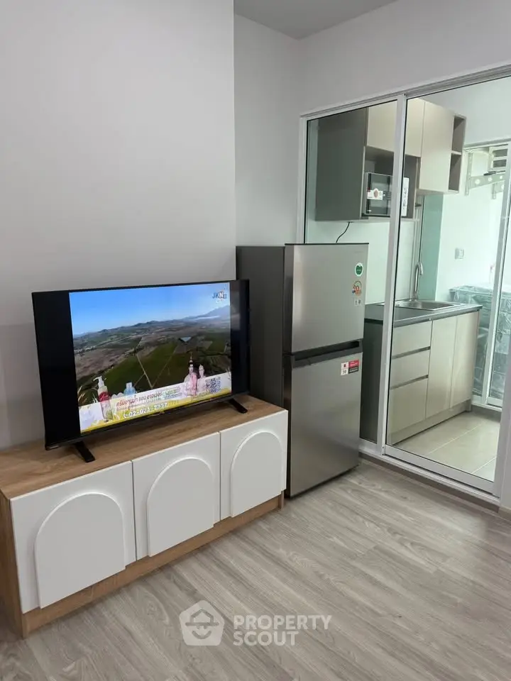 Modern living room with sleek TV unit and view into stylish kitchen with stainless steel appliances.