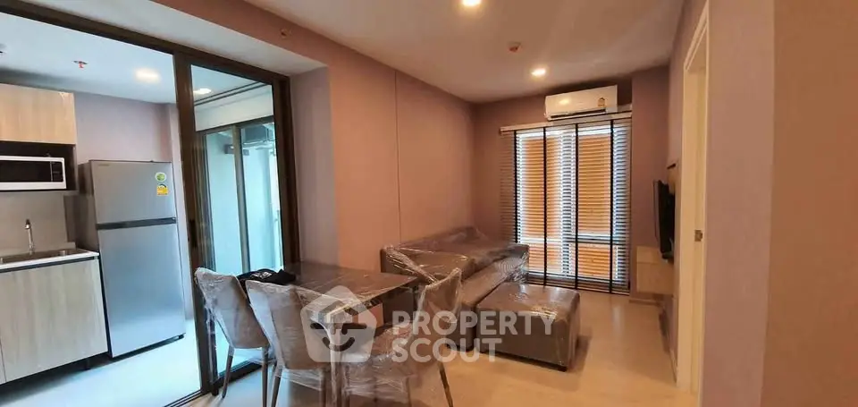 Modern living room with kitchen, featuring sleek furniture and large windows for natural light.