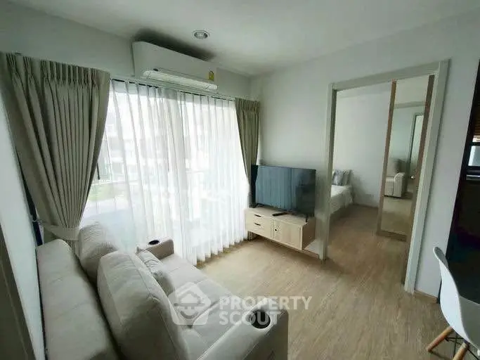 Modern living room with natural light, cozy sofa, and flat-screen TV, perfect for relaxation.