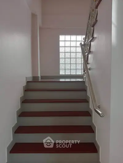 Modern staircase with sleek metal railing and glass block window.