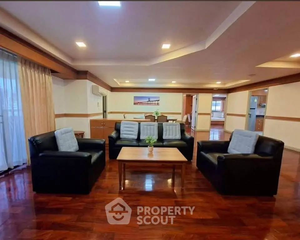 Spacious living room with elegant wooden flooring and modern black leather sofas.