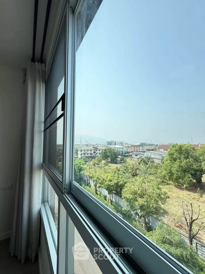Bright window view from modern apartment overlooking lush greenery and cityscape.