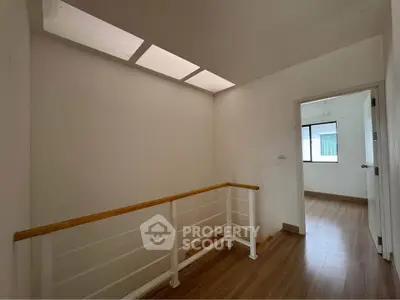 Bright hallway with wooden flooring and modern railing leading to a room with large window.