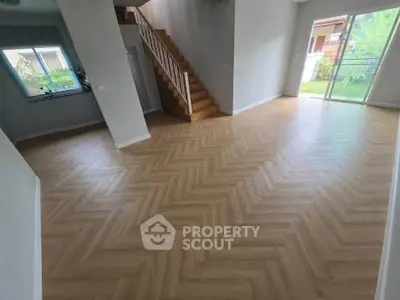 Spacious living room with elegant herringbone flooring and natural light, featuring a staircase and garden view.