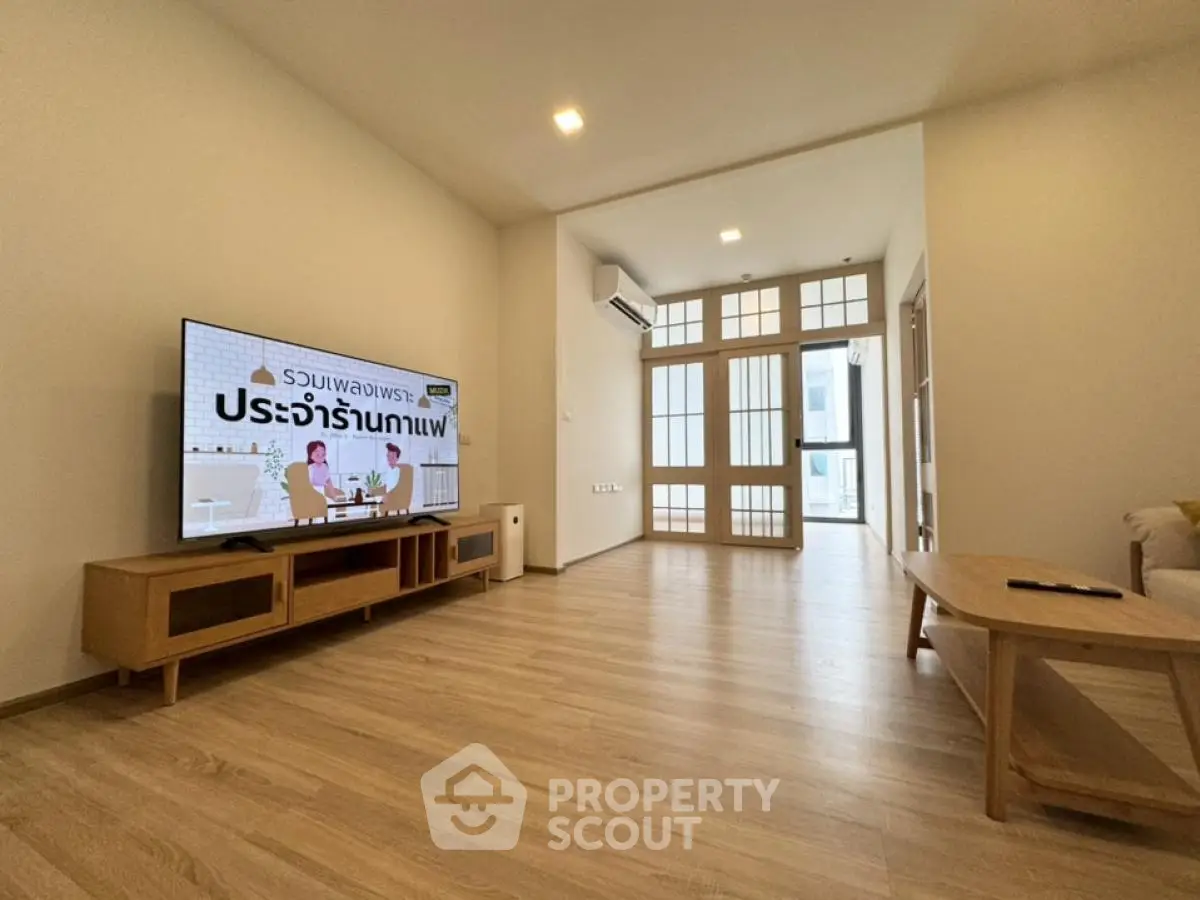 Spacious modern living room with wooden flooring and large TV, ideal for relaxation.