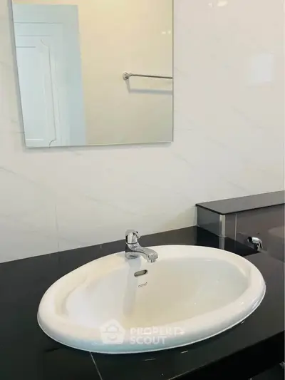 Modern bathroom with sleek sink and mirror, featuring elegant black countertop.