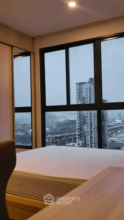Modern bedroom with large windows offering stunning cityscape views in a high-rise apartment.