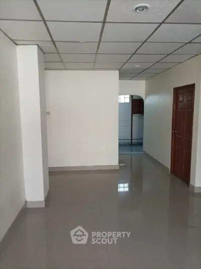 Spacious and well-lit empty interior space with glossy tiled flooring, drop ceiling, and multiple doors leading to other rooms, ideal for versatile use.