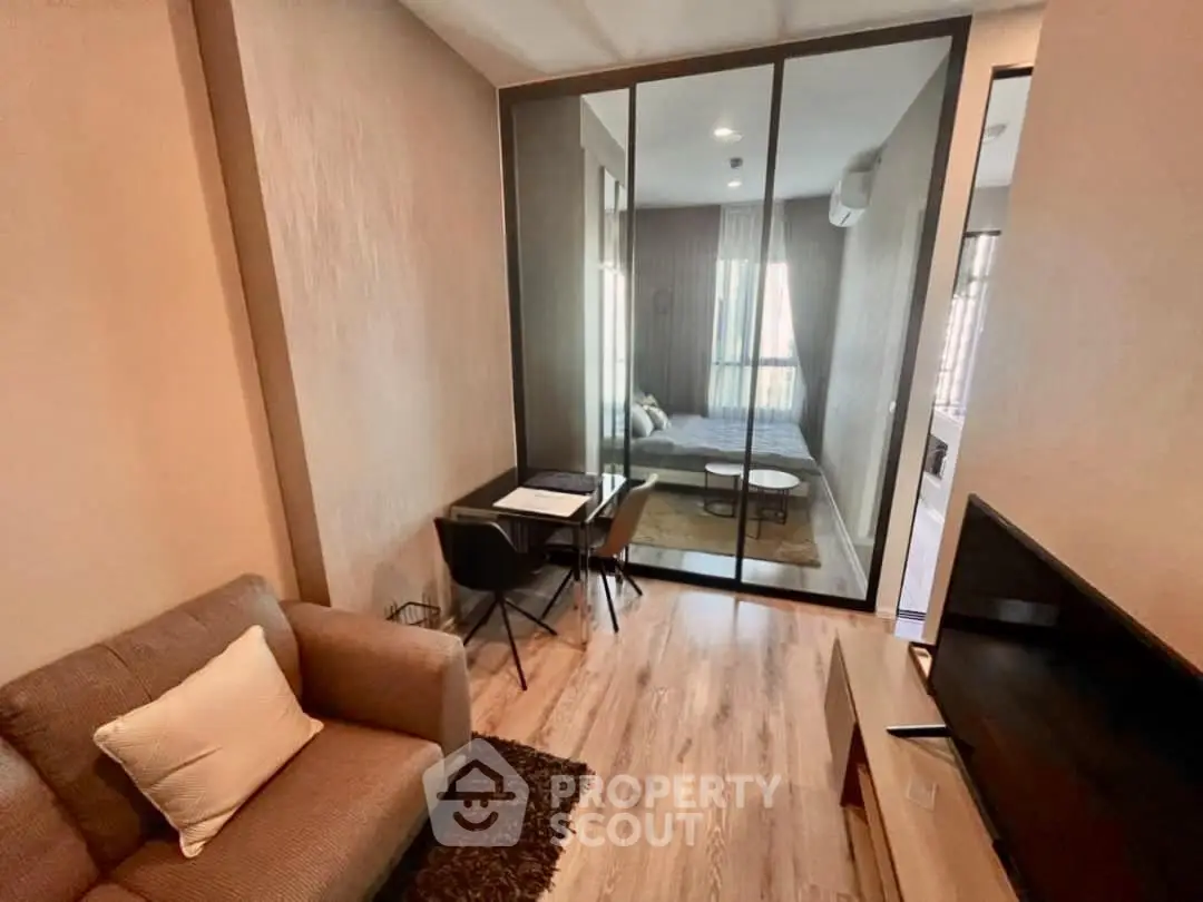 Modern living room with glass partition leading to a cozy bedroom, featuring stylish decor and natural light.