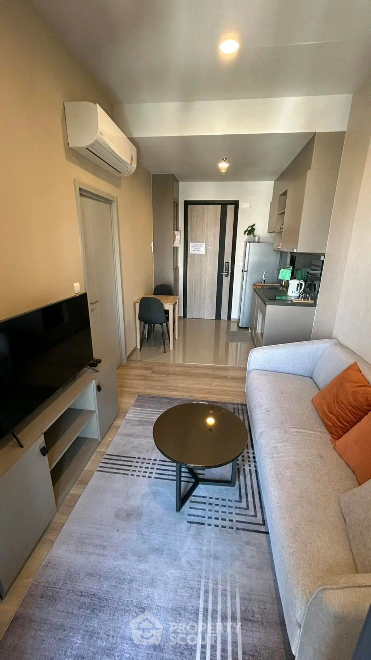 Modern living room with cozy sofa, TV, and compact kitchen in open layout apartment.