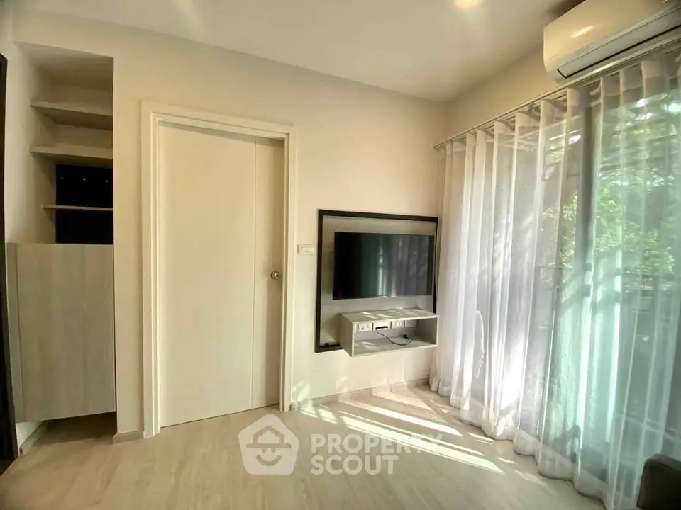 Bright living room with modern TV setup and large window with sheer curtains.