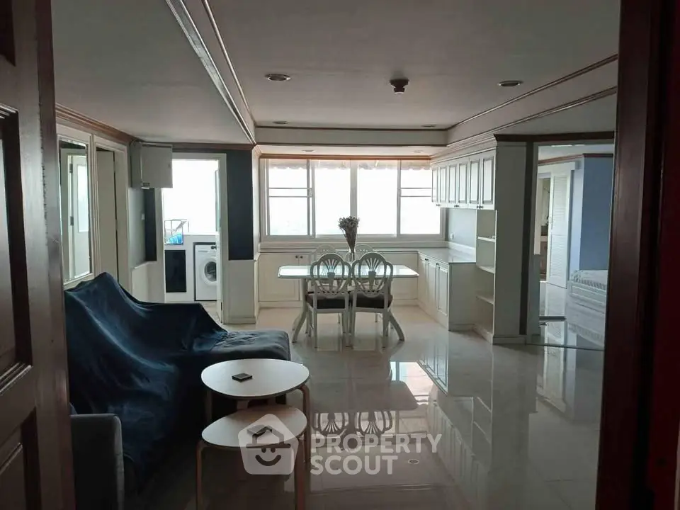 Spacious living room with dining area and washing machine, featuring modern furniture and large windows.