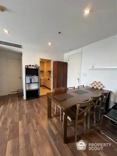 Modern dining area with wooden flooring and open kitchen layout in a stylish apartment.