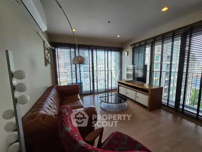 Spacious living room with modern decor and city view, featuring a leather sofa and large windows.