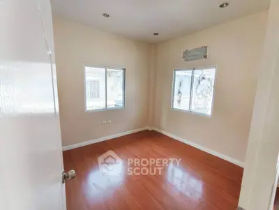 Spacious empty room with wooden flooring and large windows, perfect for customization.