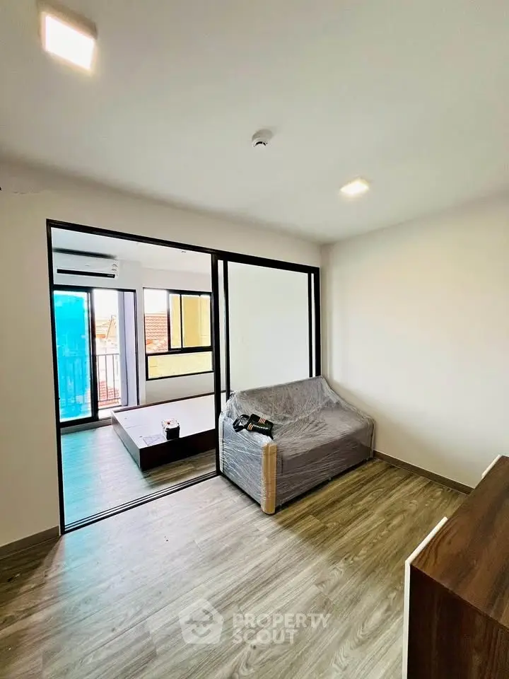 Modern living room with sliding glass doors and wood flooring, leading to a bright balcony.