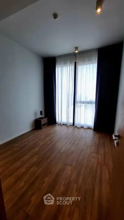 Spacious empty room with wooden flooring and large windows, perfect for customization.