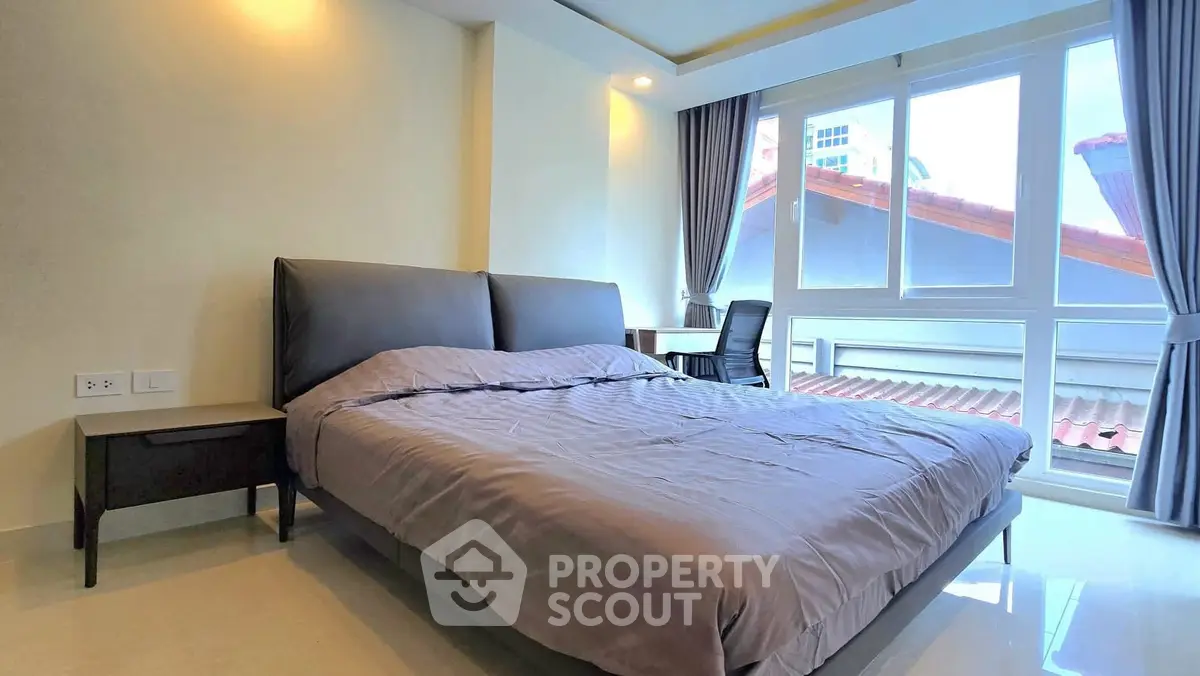 Spacious bedroom with large windows and modern furnishings in a bright apartment.