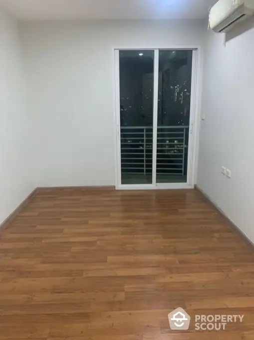 Spacious empty room with wooden flooring and balcony access in modern apartment.