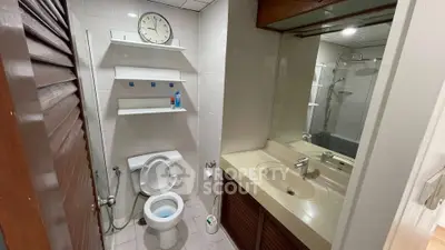Compact bathroom with toilet, sink, and shower, featuring a wall-mounted clock and shelves.