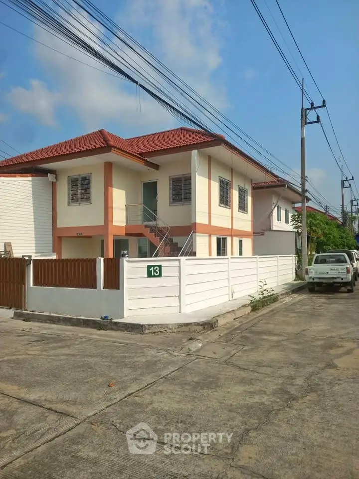 Charming two-story house with red roof and fenced yard on a sunny day.