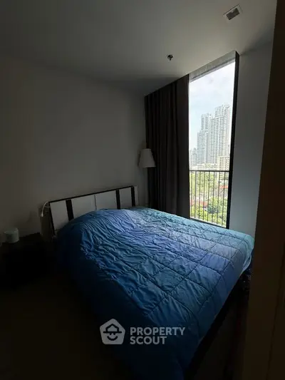 Cozy bedroom with city view, featuring a large window and modern furnishings.