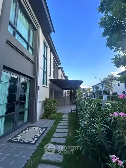 Modern townhouse exterior with lush garden and pathway, showcasing contemporary architecture and inviting outdoor space.