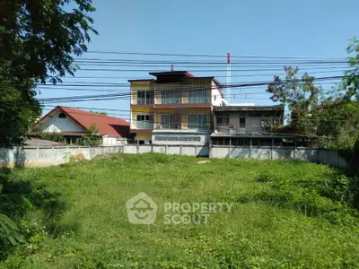 Spacious green plot with a view of a multi-story building, ideal for development.