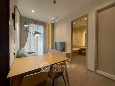 Modern living room with dining area and view into bedroom, featuring sleek furniture and natural lighting.