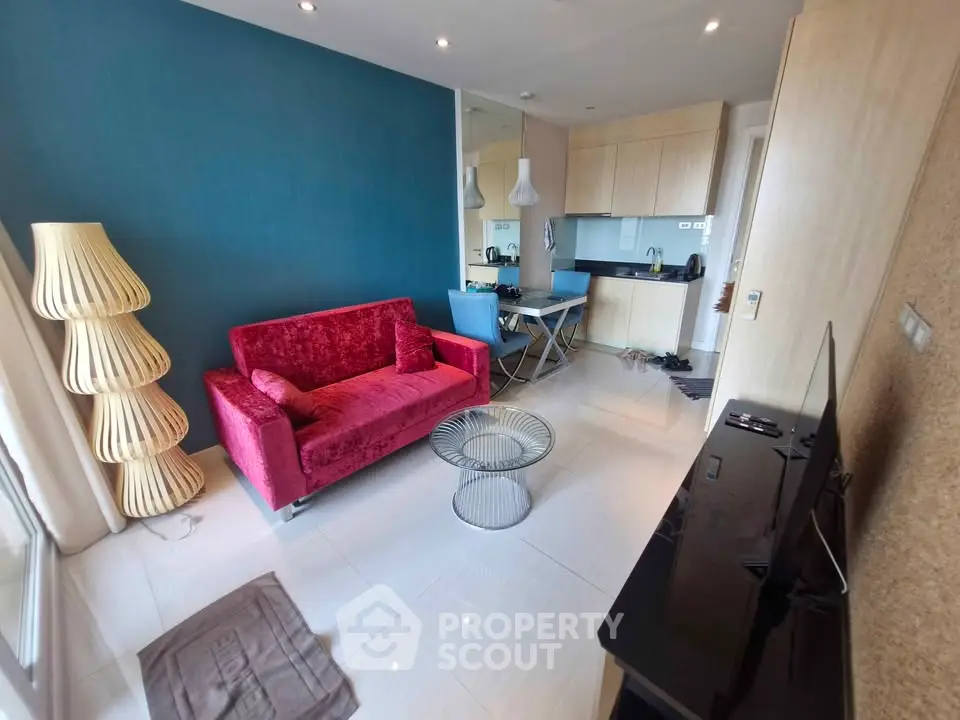 Modern living room with vibrant red sofa and sleek kitchen area, perfect for urban living.