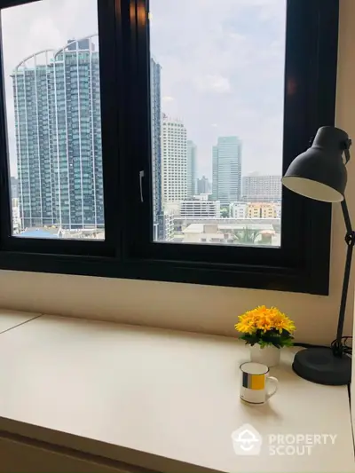 Modern study room with city view, featuring a sleek desk, lamp, and decorative plant.