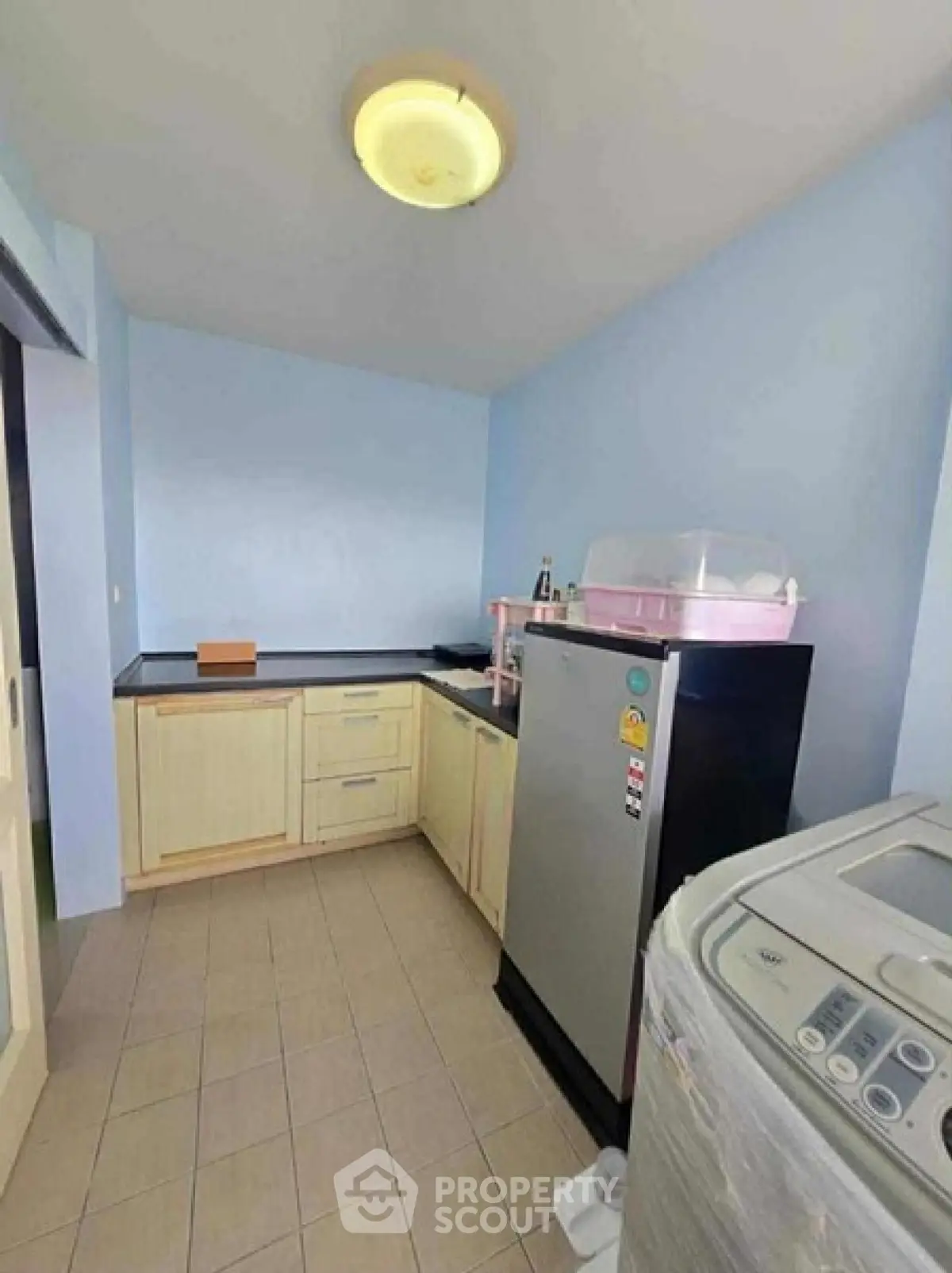 Compact kitchen with modern appliances and light blue walls, featuring a washing machine and refrigerator.