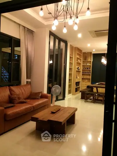 Spacious living room with modern lighting and open layout, featuring a cozy leather sofa and wooden accents.