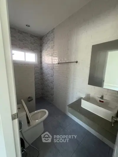 Modern bathroom with sleek fixtures and tiled walls, featuring a large mirror and natural light.