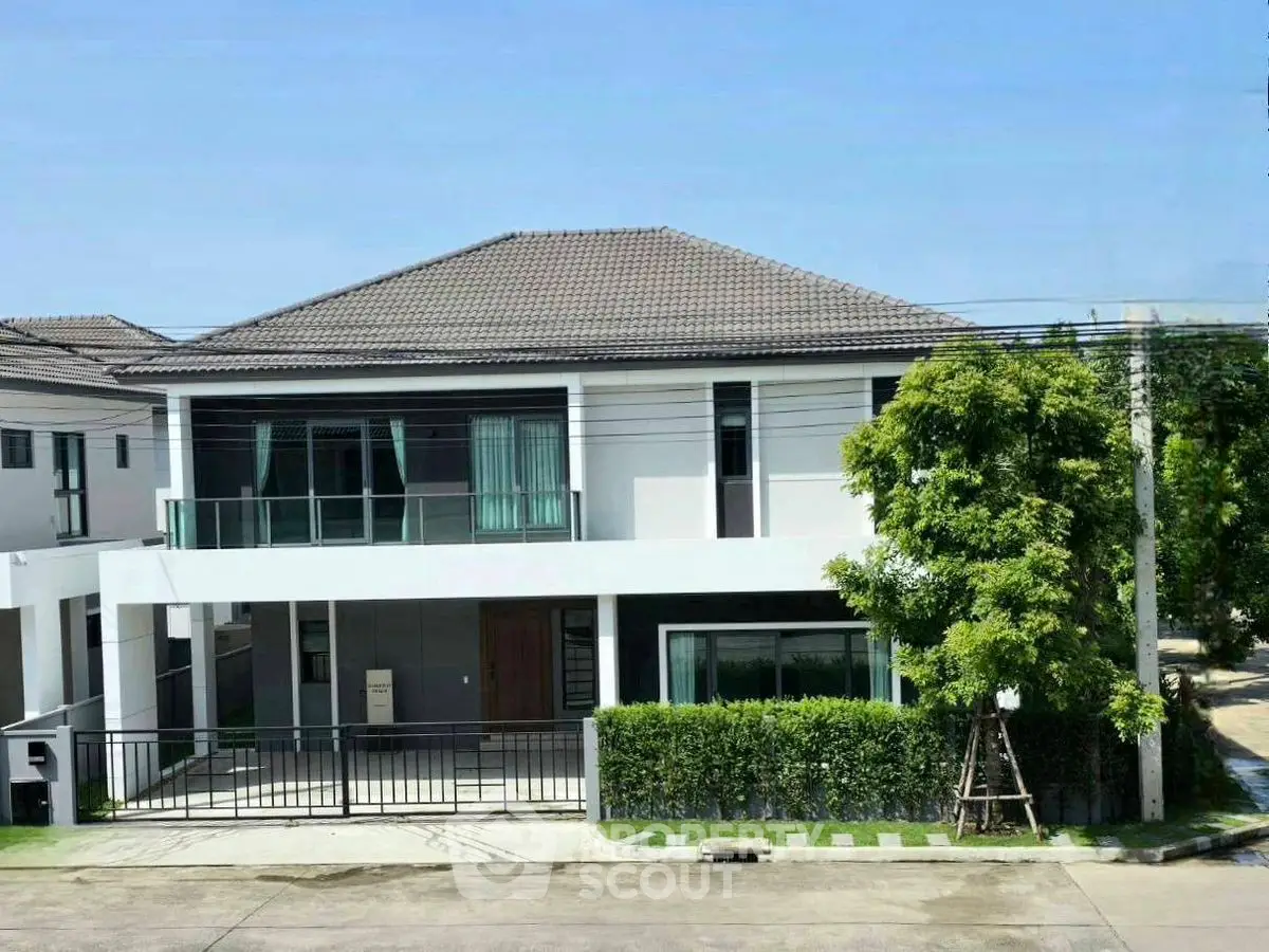 Modern two-story house with spacious balcony and lush greenery in suburban neighborhood.