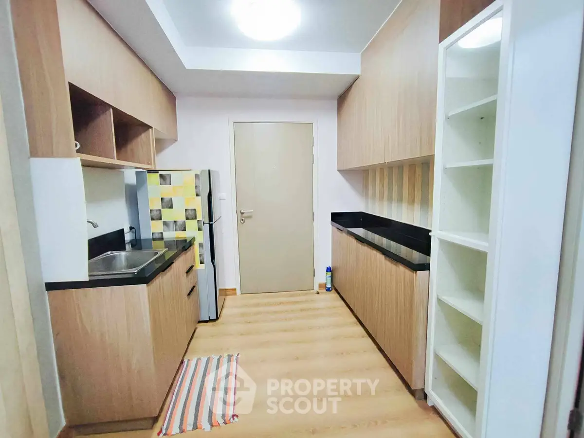 Modern kitchen with sleek cabinetry and wood flooring, featuring a compact fridge and stylish backsplash.