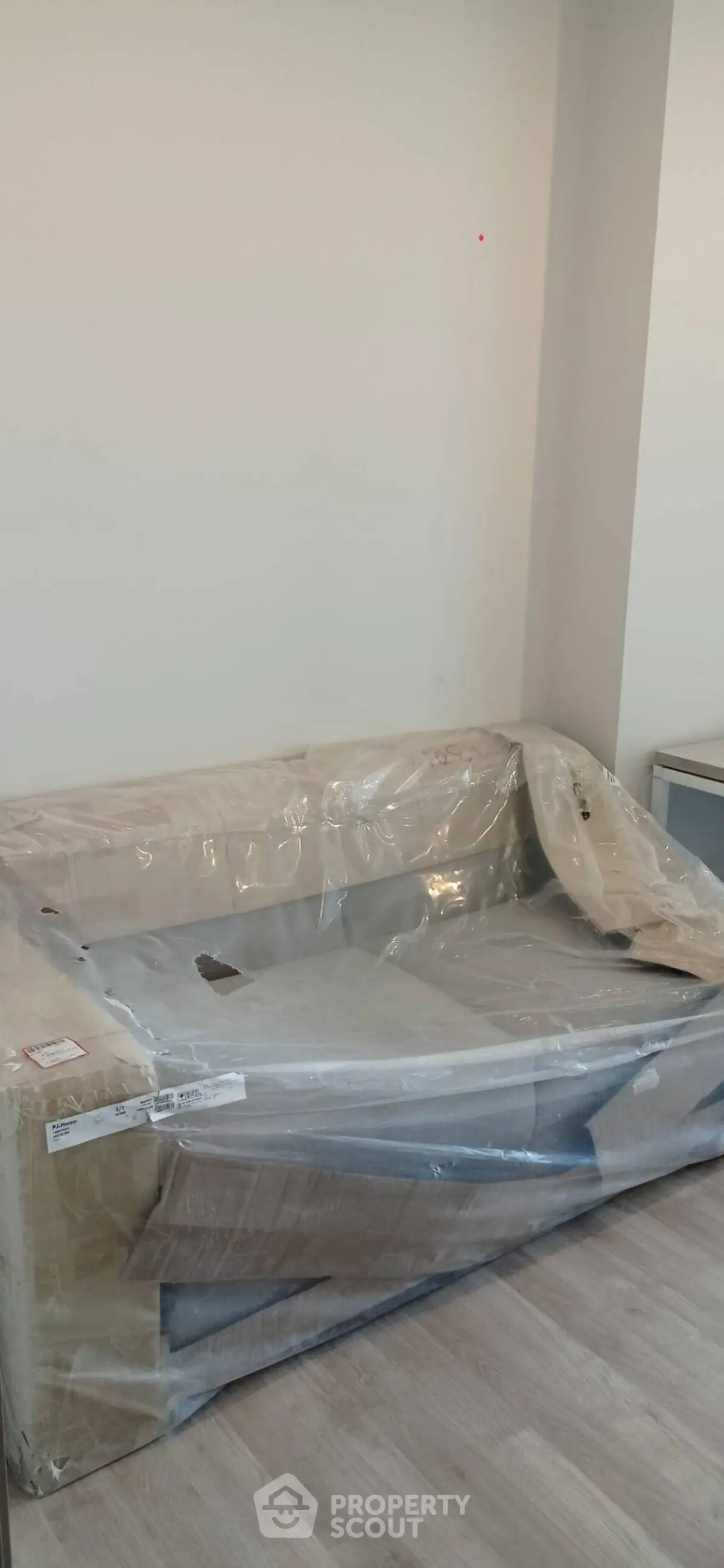 Modern living room with new sofa wrapped in protective plastic, showcasing sleek wooden flooring.