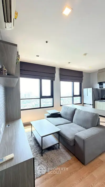 Modern living room with city view, stylish gray sofa, and sleek kitchen area.