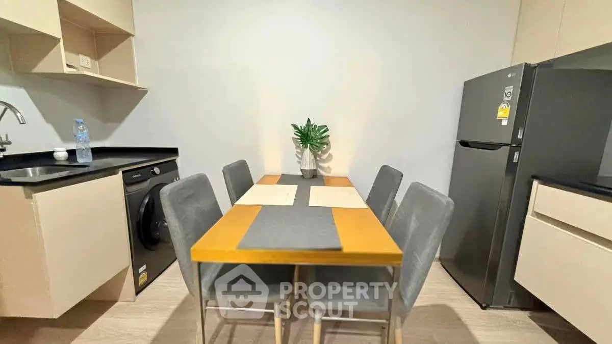 Modern kitchen with dining table, washing machine, and fridge in sleek apartment.