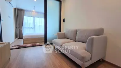 Modern apartment interior with cozy living room and bedroom separated by glass sliding door.