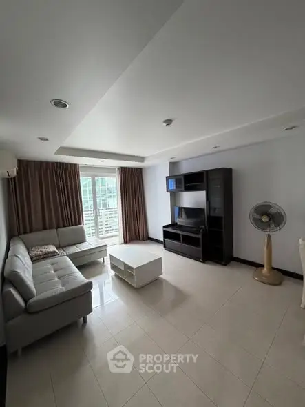 Spacious living room with modern sofa and entertainment unit, featuring large windows for natural light.