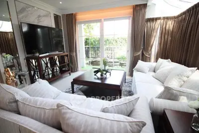 Luxurious living room with elegant sofas and large TV, opening to a lush garden view.