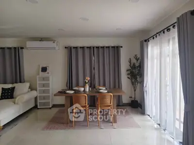 Elegant living room with dining area, featuring modern furniture and large windows with curtains.