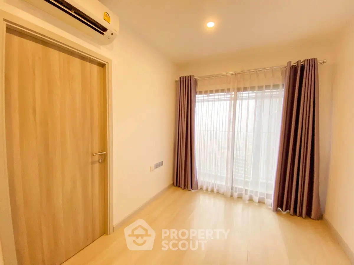 Bright empty room with wooden floor, air conditioning, and large window with curtains.