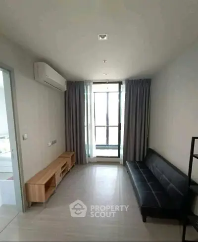 Modern living room with sleek black sofa and natural light from large window.